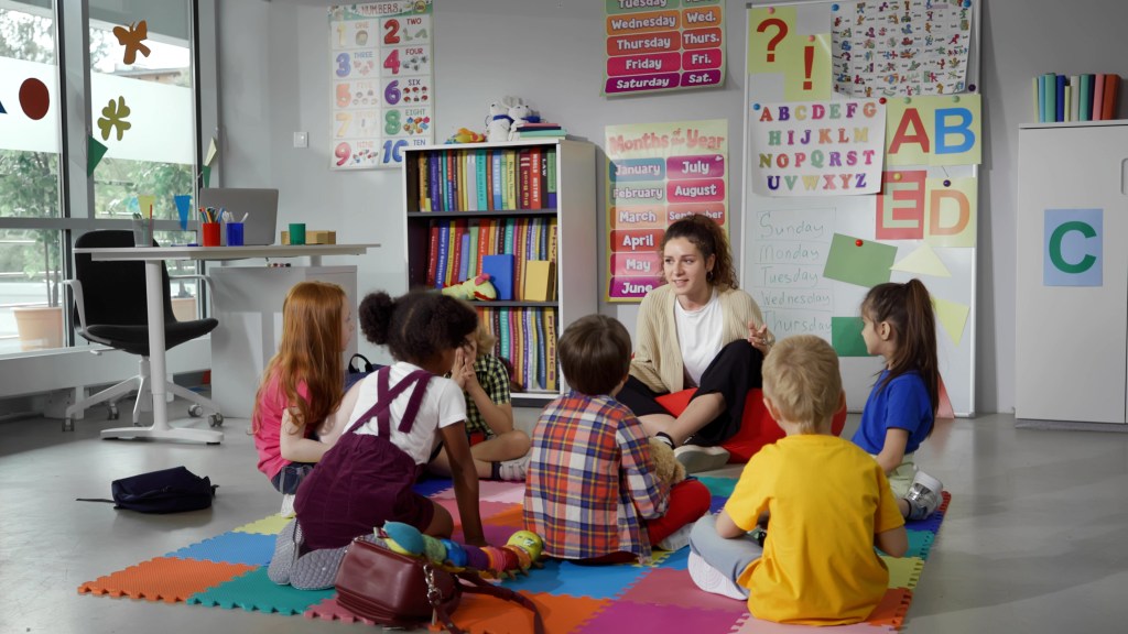 Young teacher sitting on the floor during a lesson with young kindergarten children